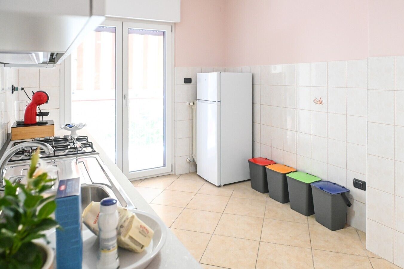 A kitchen with a gas stove, a refrigerator, and four waste bins.