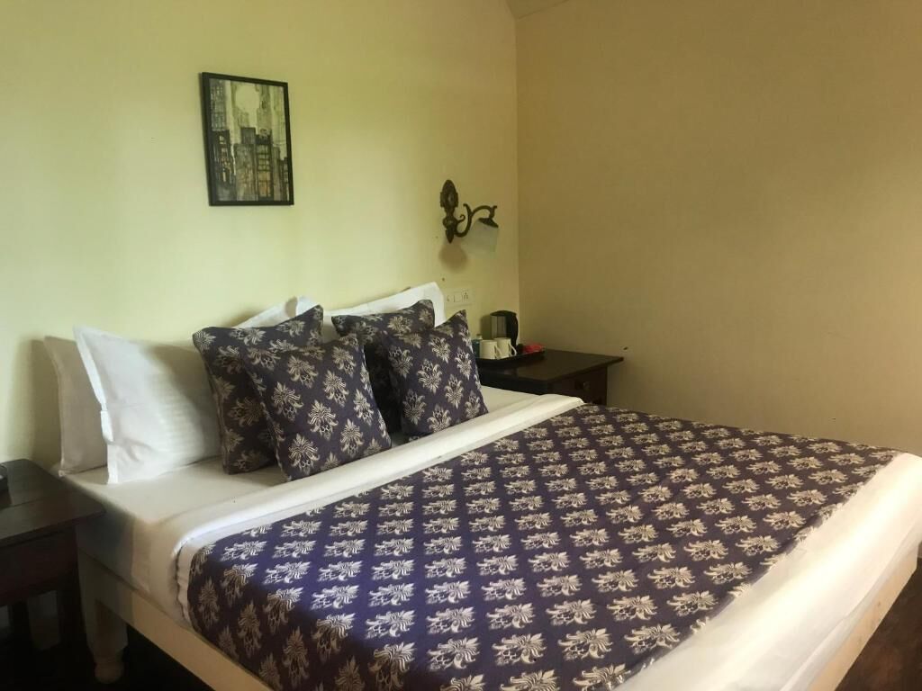 Una cama con una colcha estampada, una mesita de noche con una lámpara y un cuadro colgado en la pared.