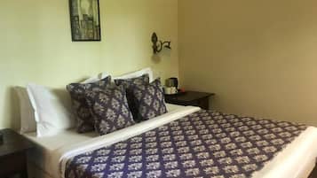 Una cama con una colcha estampada, una mesita de noche con una lámpara y un cuadro colgado en la pared.