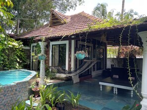 A house with a swimming pool, a hammock, and potted plants.
