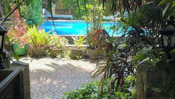 Un espace piscine agrémenté d’un chemin dallé menant à la piscine, le tout entouré d’une végétation luxuriante et de plantes en pot.