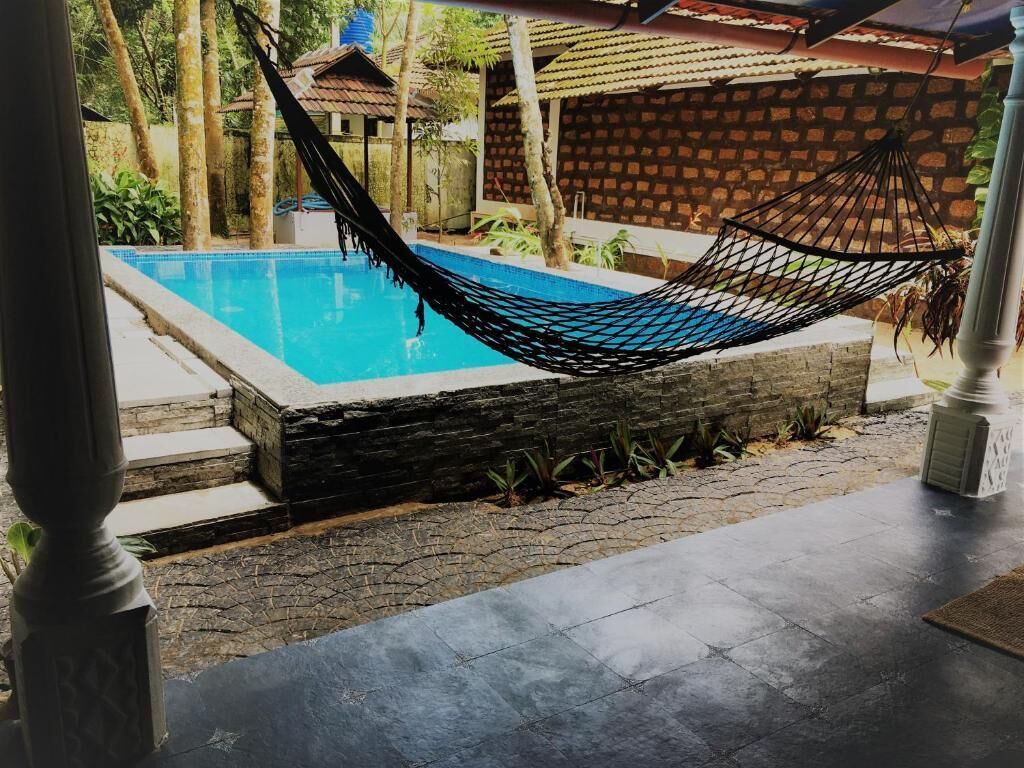 Una hamaca sobre una piscina con un muro de piedra y una estructura de techo con tejas al fondo.