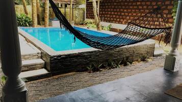 Una hamaca sobre una piscina con un muro de piedra y una estructura de techo con tejas al fondo.