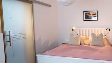 Een slaapkamer met een wit bed, een witte kledingkast en een aan de muur hangend schilderij.