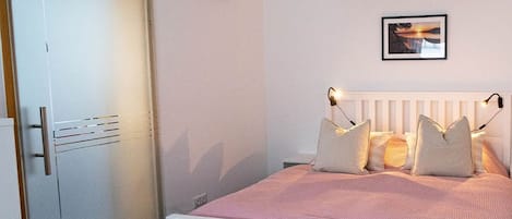 Ein Schlafzimmer mit einem weißen Bett, einem weißen Kleiderschrank und einem an der Wand hängenden Bild.