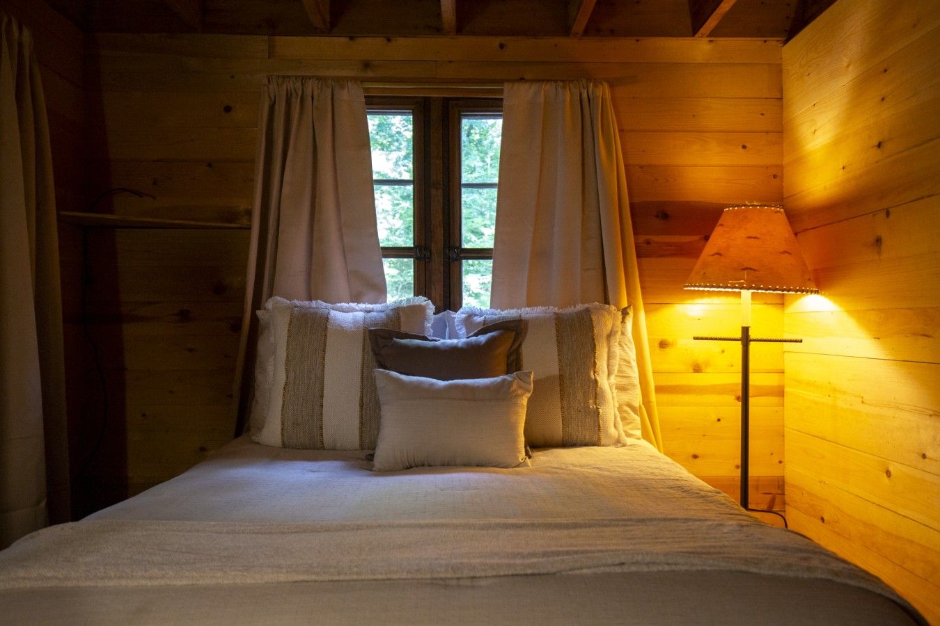 Ein Zimmer in einer Holzhütte mit einem Bett, Vorhängen und einer Lampe.
