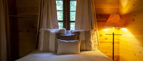Una habitación de cabaña de madera con una cama, cortinas y una lámpara.