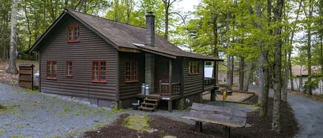 A rustic cabin with a porch, a chimney, and a small deck area.