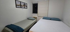 A small, single-room accommodation with two beds, a window with bars, and a wall-mounted picture. - Decorated corner near the beach in Jardim Camburi (Vitória)
