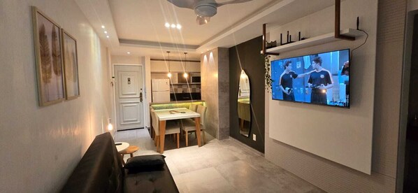 Ein modernes Wohnzimmer mit Flachbildfernseher an der Wand, einem Essbereich mit Tisch und Stühlen und einer Couch.