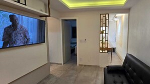 A hallway with a television, a black sofa, and framed leaves on the wall. - Decorated corner near the beach in Jardim Camburi (Vitória)