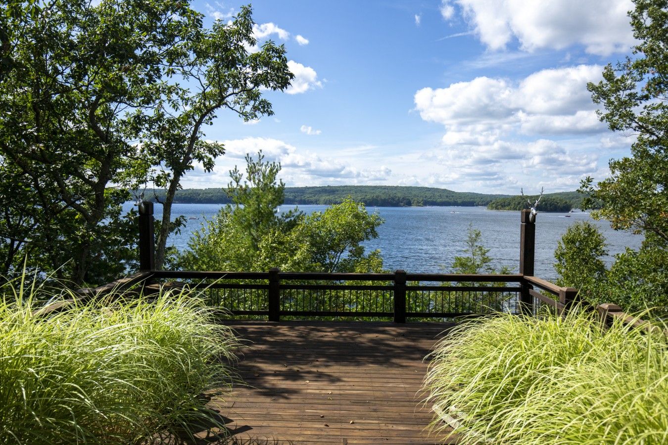 Eine Holzterrasse, die zu einem See führt, mit freiem Blick auf das Wasser und sanfte Hügel in der Ferne.