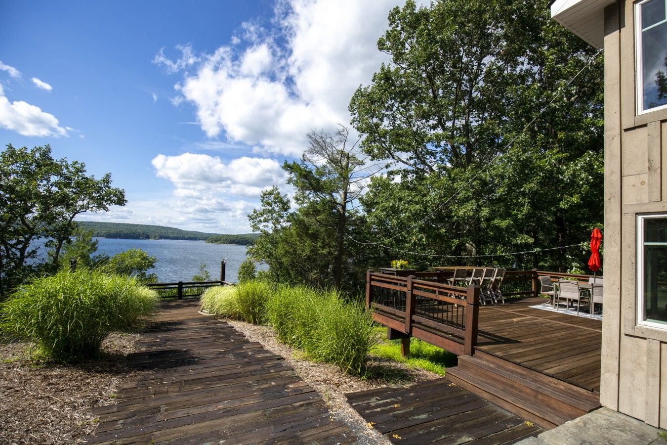 A wooden deck leading to a lakeside property with a view of the lake and distant hills.