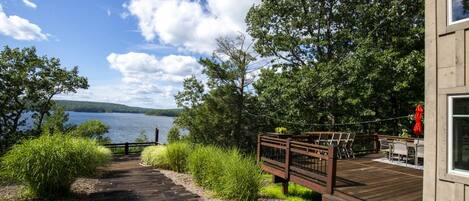 A wooden deck leading to a lakeside property with a view of the lake and distant hills.