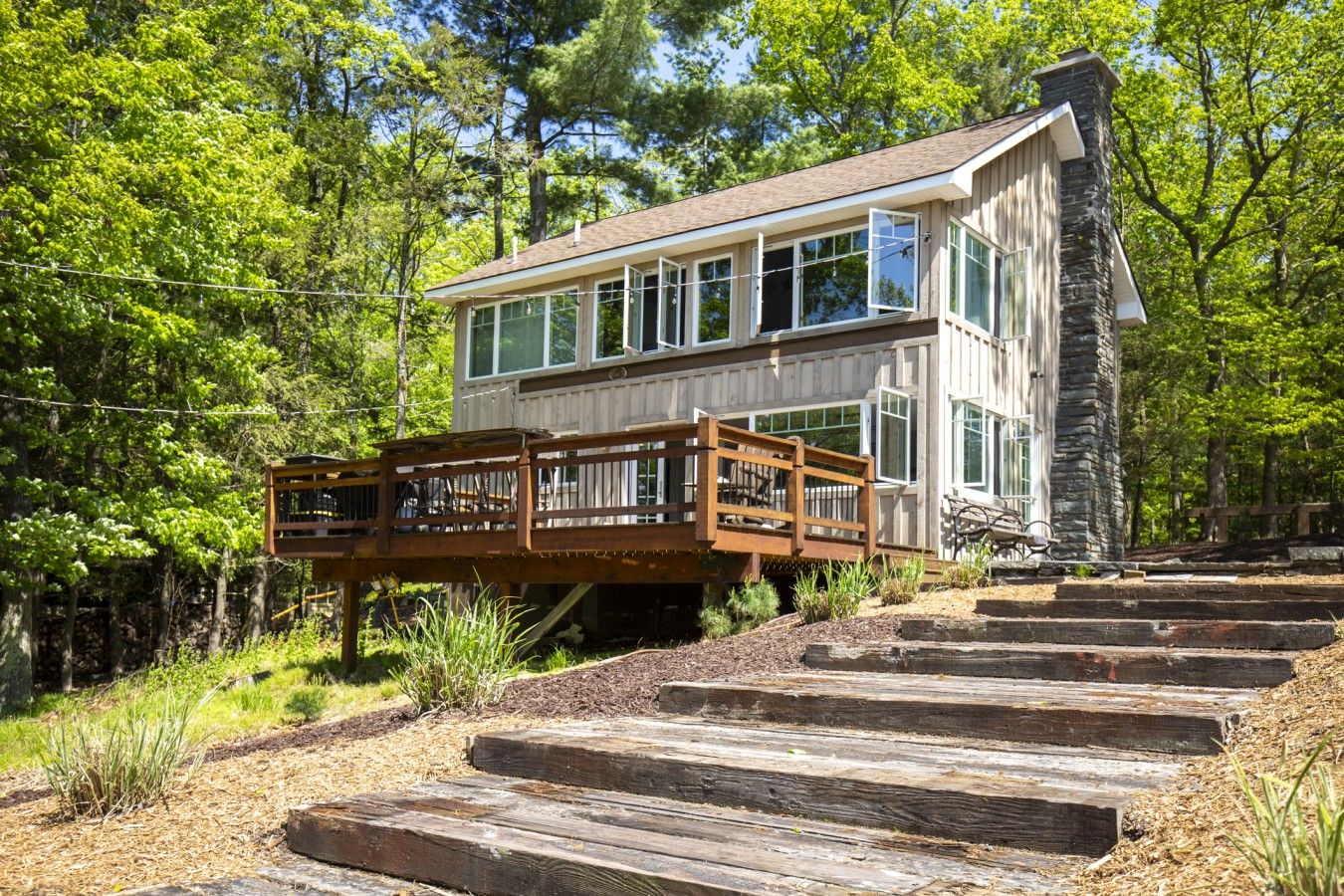 Ein zweistöckiges Holzhaus mit einem Steinsschornstein, einer Terrasse und einer Treppe, die zum oberen Stockwerk führt.