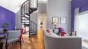Una sala de estar moderna con una escalera en espiral, sofás grises y un papel tapiz de diseño pata de gallo.
