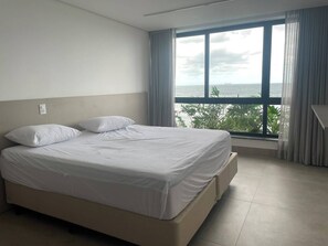 A hotel room with a bed, a window with curtains, and a view of the sea. - Beachfront House in Maresias | Private Pool | Oceanfront (São Sebastião)