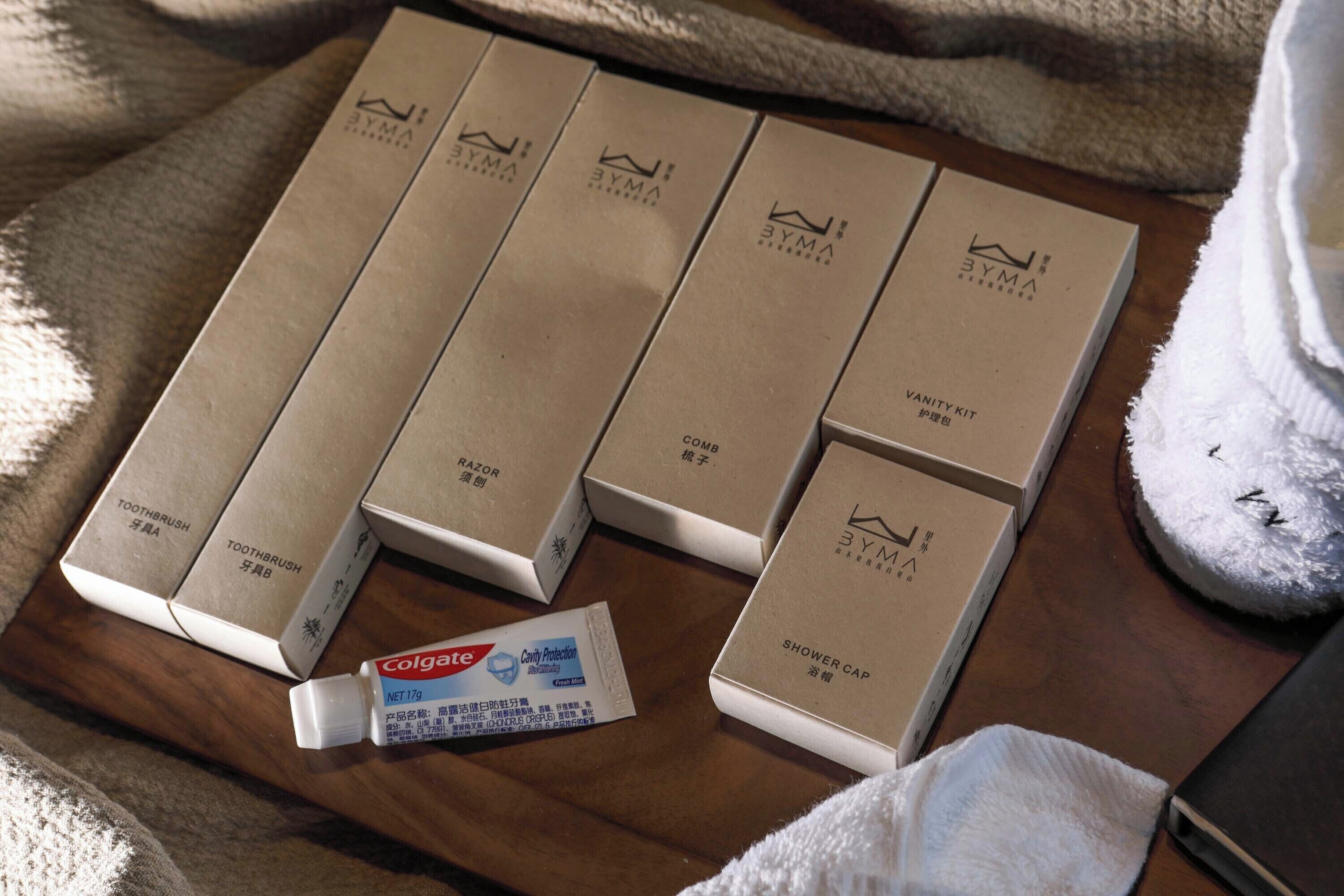 A wooden surface with several brown boxes labeled '3YMA' and 'TOOTHBRUSH' alongside a tube of Colgate toothpaste.
