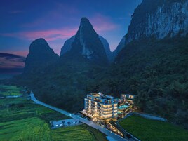 Un hotel moderno de varios pisos, rodeado de exuberante vegetación y montañas.