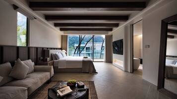 A modern hotel room with a large bed, a sofa, a coffee table with a magazine, and a view of the outdoors.