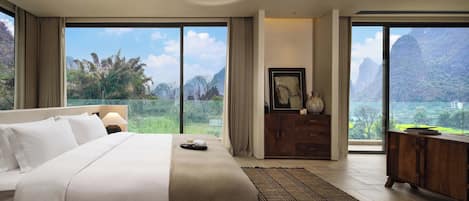 A hotel room with a large bed, a desk, and a view of mountains through the windows.