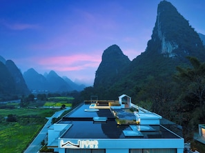 A modern building with a flat roof, surrounded by mountainous terrain and a river. - BYMA Valley Hideaway Resort Yangshuo·Ten-Mile Gallery · Yulong River·Double-Level Cliffside Infinity Pools (Guilin)