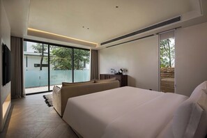 A modern hotel room with a large bed, a sofa, a flat-screen TV, and a sliding glass door leading to a balcony.