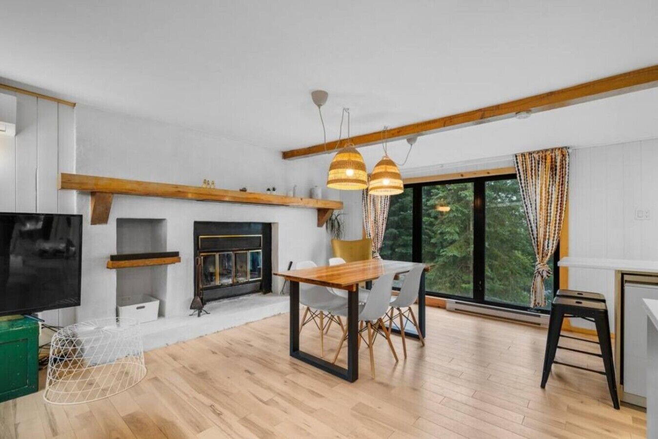 A modern living room with a fireplace, wooden beams, a dining table, and a large window.