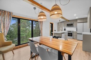 Una cocina moderna con una isla central, un comedor con mesa y sillas de madera, y ventanas amplias que ofrecen vistas al exterior.