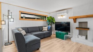 A modern living room with a sectional sofa, a flat-screen TV, a green storage unit, and a plant.