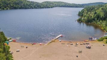 Une plage au bord d’un lac, avec un quai, des bateaux et une zone sablonneuse dotée de bancs.