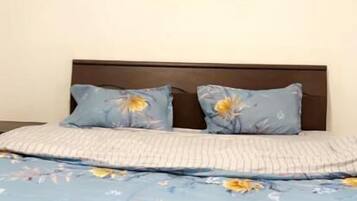 Un letto con una coperta a fiori, due cuscini con un motivo a margherita e un quadro raffigurante un tramonto appeso al muro.
