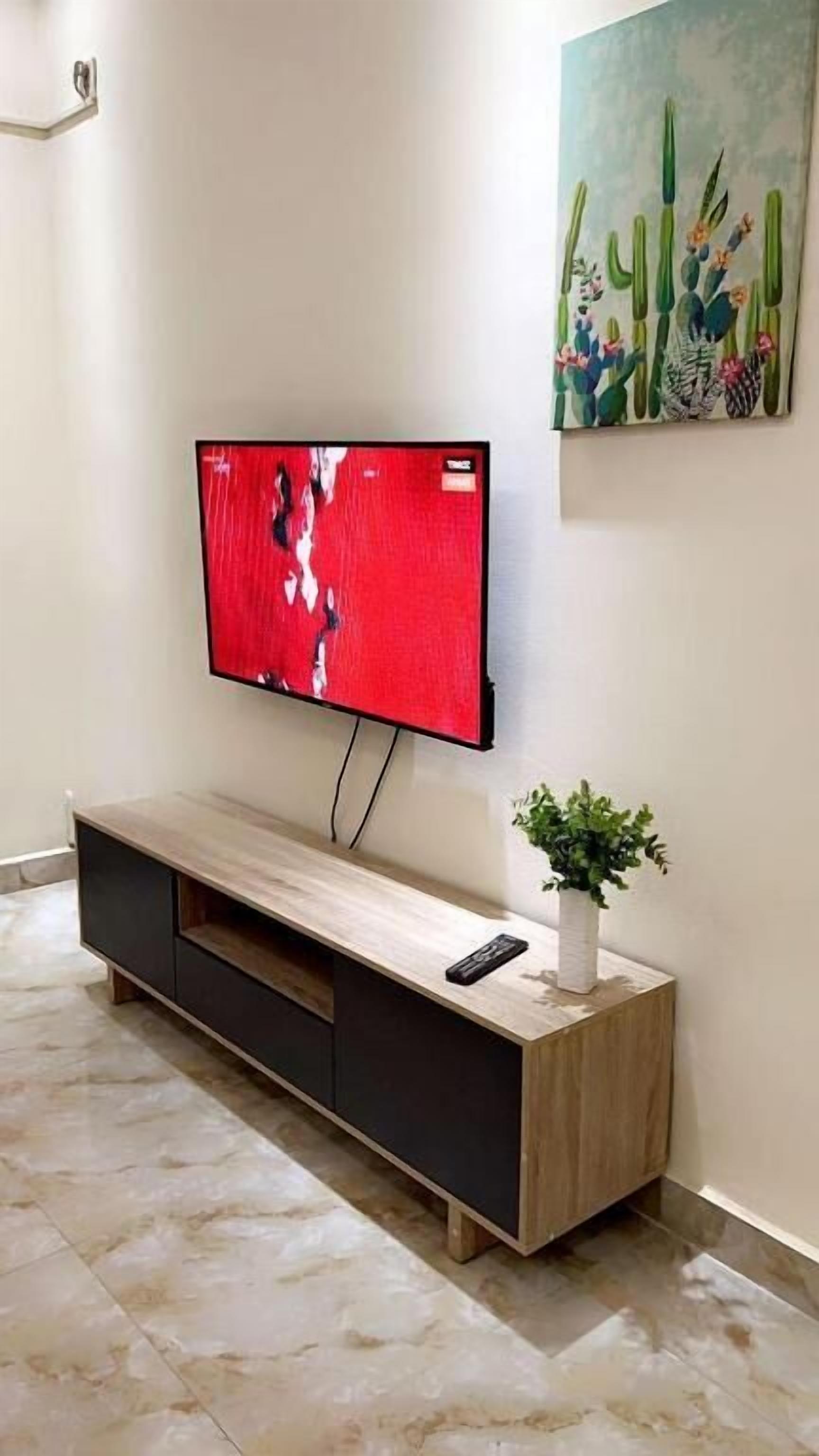 Televisão de tela plana fixada na parede sobre um console de madeira com gavetas.