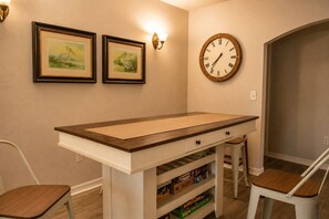 Ein Zimmer mit einem langen Tisch, zwei Stühlen, einer Wanduhr und gerahmten Bildern.