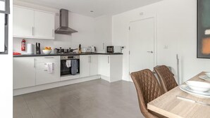 A modern kitchen with white cabinets, a stove, and a microwave. There is a dining table with chairs and a fire extinguisher on the wall. - Luxurious Stockport Retreat - 4 Bedrooms (Stockport)