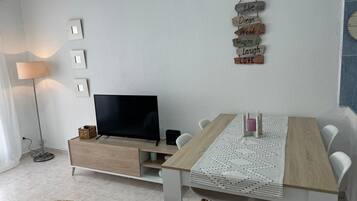 A modern living room with a flat-screen TV, a wooden dining table, and a wall-mounted sign with motivational phrases.