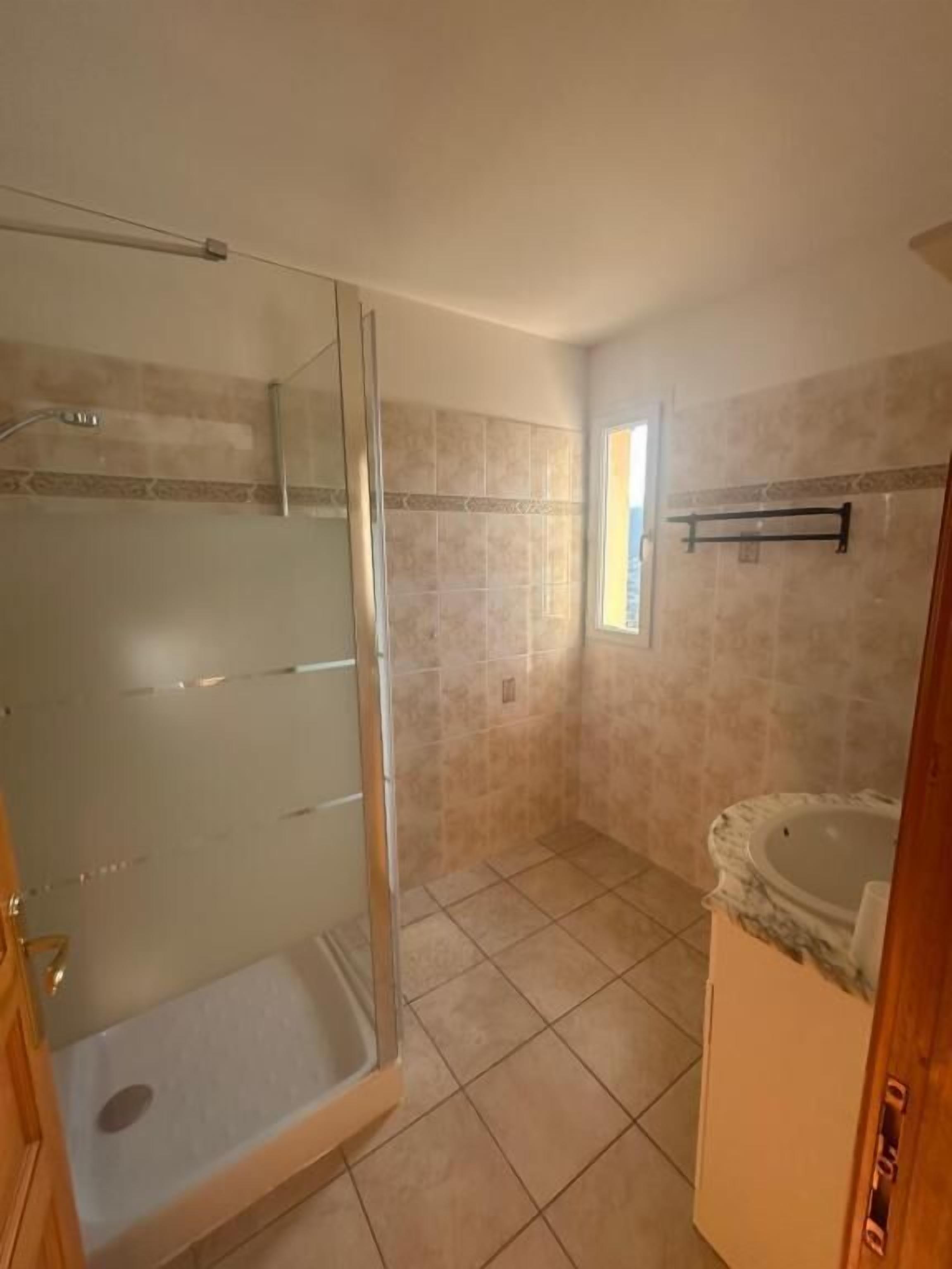 A bathroom with a glass-enclosed shower, a bathtub, and a window providing natural light.