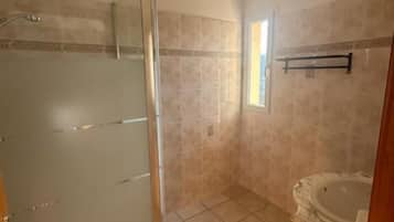 A bathroom with a glass-enclosed shower, a bathtub, and a window providing natural light.