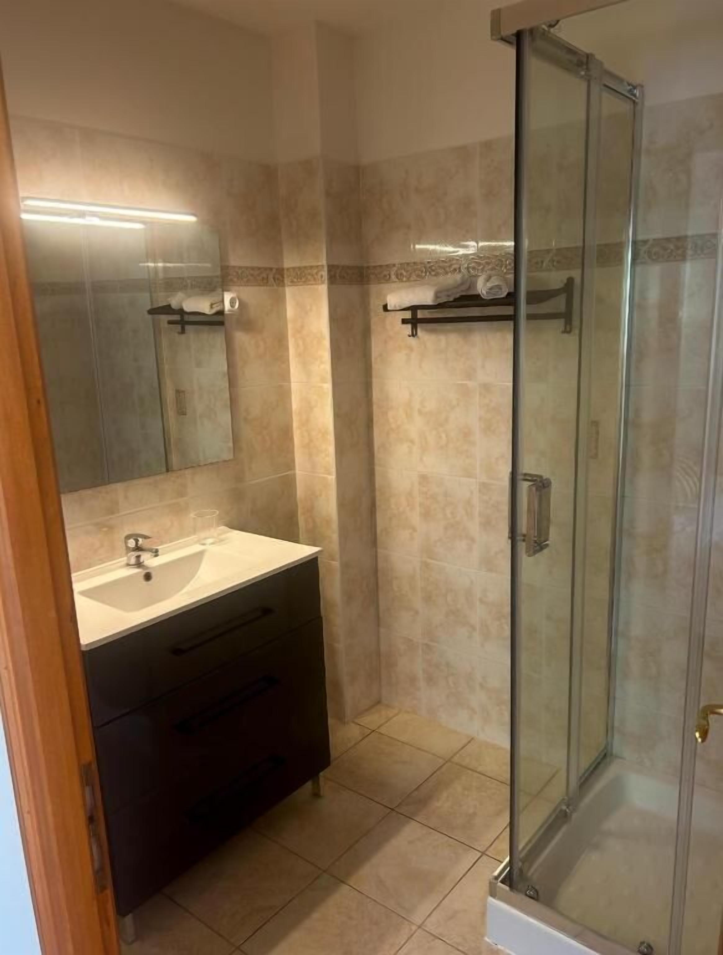 A bathroom with a glass-enclosed shower, a vanity with a sink, and a mirror.