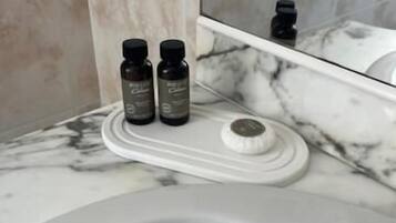 Baño con encimera de mármol, lavamanos blanco y dos botellas pequeñas sobre una bandeja.