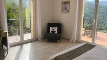 Une chambre à coucher avec un lit, une petite table et une chaise. Il y a un balcon avec vue sur l’extérieur.