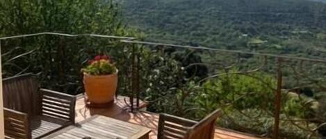 A terrace with a table and chairs, overlooking a mountainous landscape.