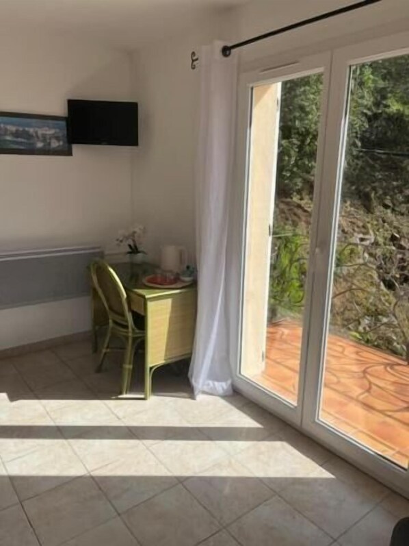 A room with a dining table and chairs, a TV mounted on the wall, and a sliding glass door leading to an outdoor area.