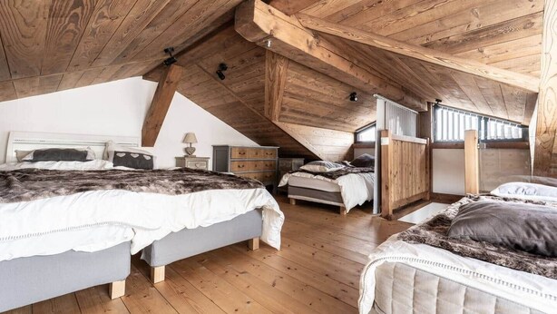 Ein Schlafzimmer mit schrägen Wänden, Holzbalken, einem Bett mit Felldecke, einem Nachttisch mit Lampe und einer Kommode.