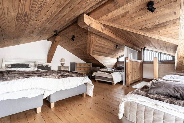 Ein Schlafzimmer mit schrägen Wänden, Holzbalken, einem Bett mit Felldecke, einem Nachttisch mit Lampe und einer Kommode.