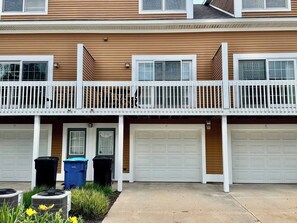 A two-story residential building with a balcony, two garages, and trash bins. - Watermark | 3BR Retreat | Balcony | Fireplace (Saugatuck)