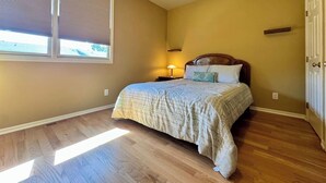 A bedroom with a bed, a nightstand, a lamp, a window with blinds, and a ceiling fan. - Watermark | 3BR Retreat w/ Balcony | Water View (Saugatuck)