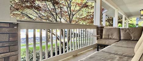 A covered porch with a cushioned seating area and a view of trees.