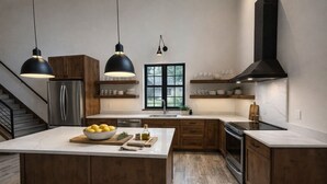 Eine moderne Küche mit Holzschränken, einer zentralen Kochinsel, Edelstahlgeräten und Pendelleuchten sowie einem großen Fenster.