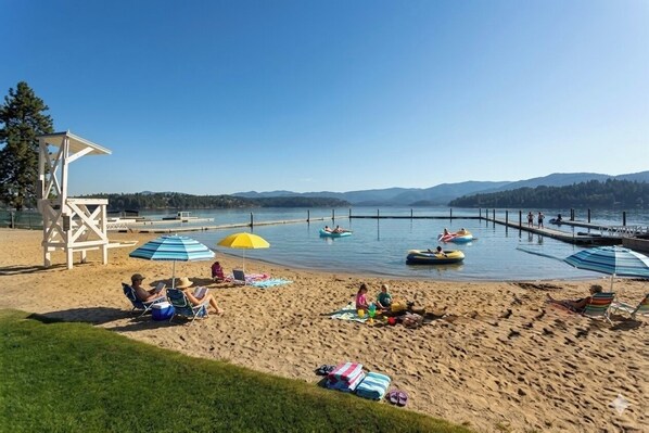 A beach with lounge chairs, umbrellas, and a lifeguard tower. - Private Pickleball Court, Luxury New Build, Sleeps 8 (Hayden Lake)